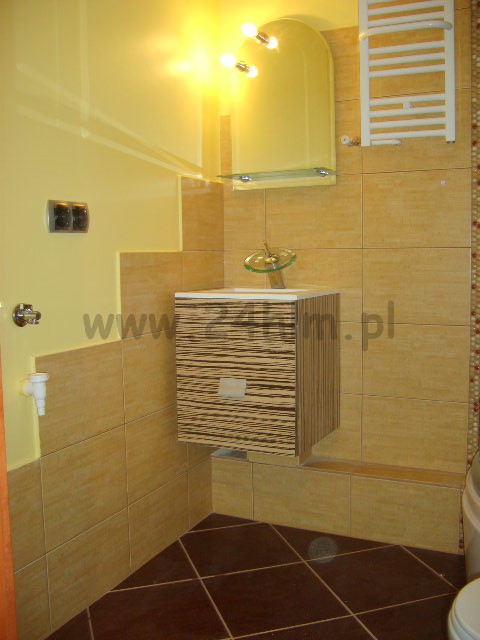 Ukończona łazienka z beżowymi płytkami, brązową podłogą, wiszącą szafką z umywalką o wzorze zebry i grzejnikiem drabinkowym.